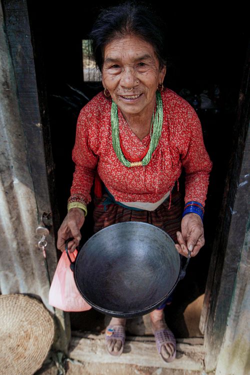 Free Smiling elderly woman in colorful attire holding a pot at a doorway, showcasing cultural traditions. Stock Photo