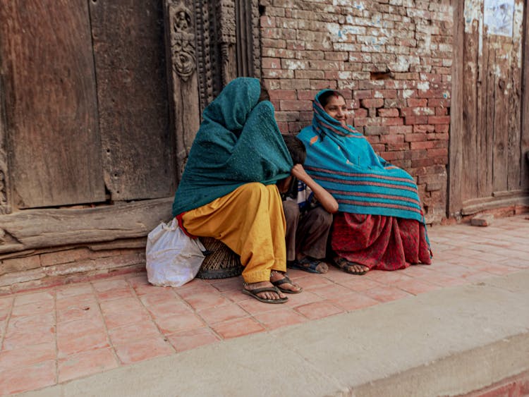 Women In Headscarves And A Child Sitting Outside A Building 