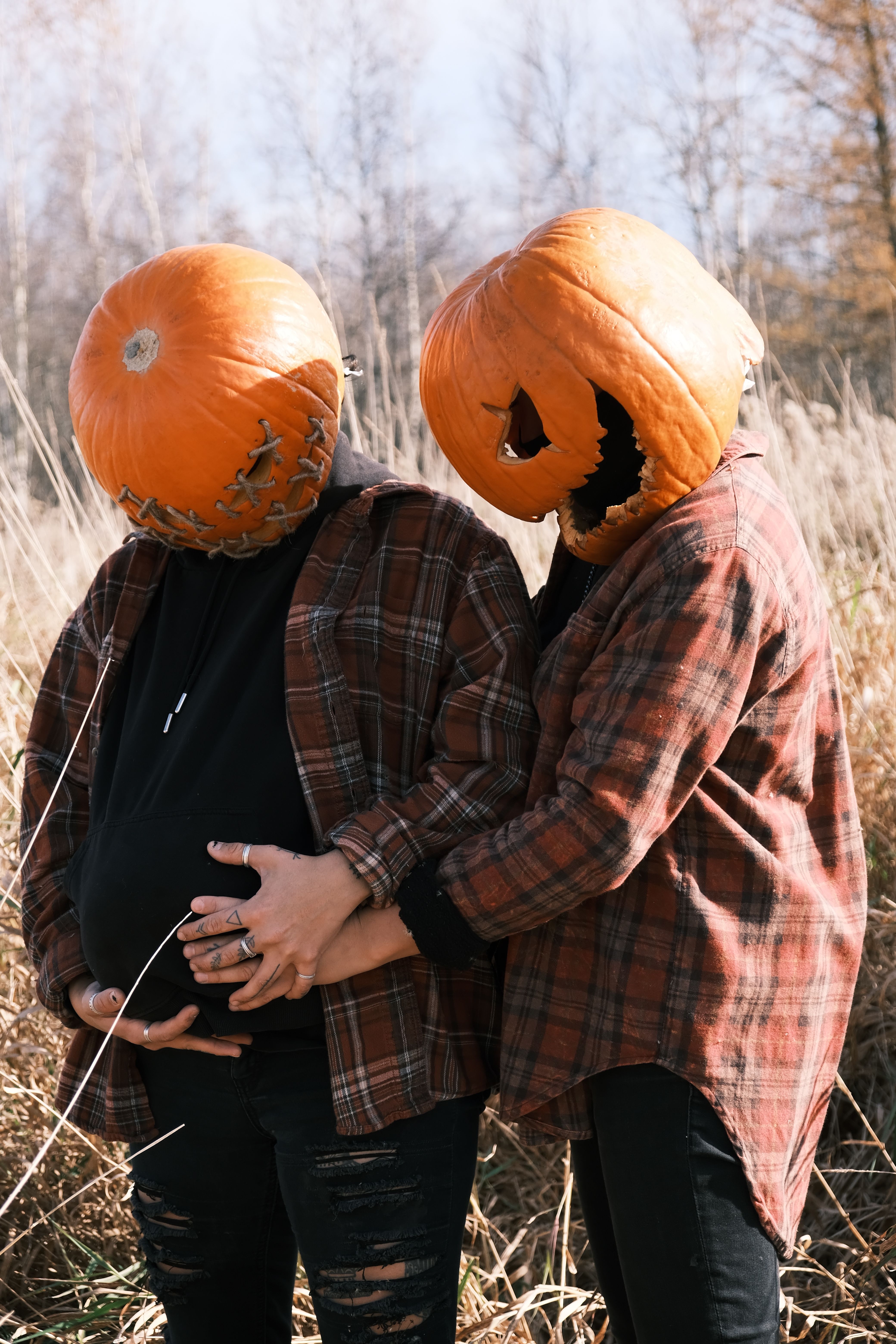 A couple wearing pumpkin heads and plaid shirts in a rural autumn setting.
