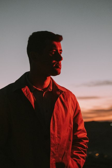 A man in a button-up shirt gazes into the sunset, creating a striking silhouette.