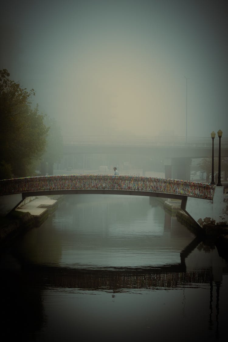 Person Crossing Bridge Above Water In Fog