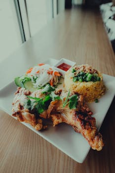 Plate of Asian fusion cuisine featuring grilled chicken, fried rice, and fresh vegetables.