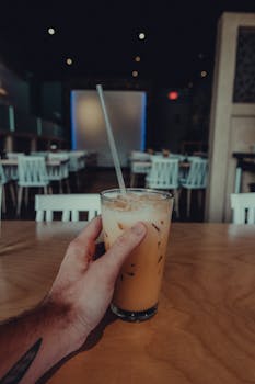 A person holding a glass of iced Thai tea inside a cozy, vintage-style cafe.