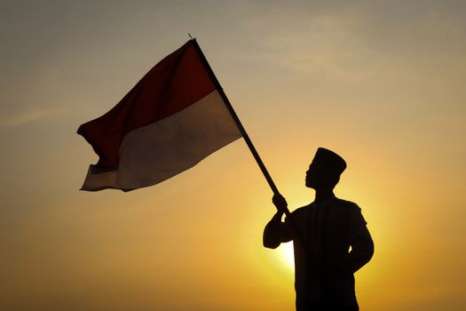 Silhouette of individual waving Indonesian flag during a vibrant sunset, symbolizing national pride.