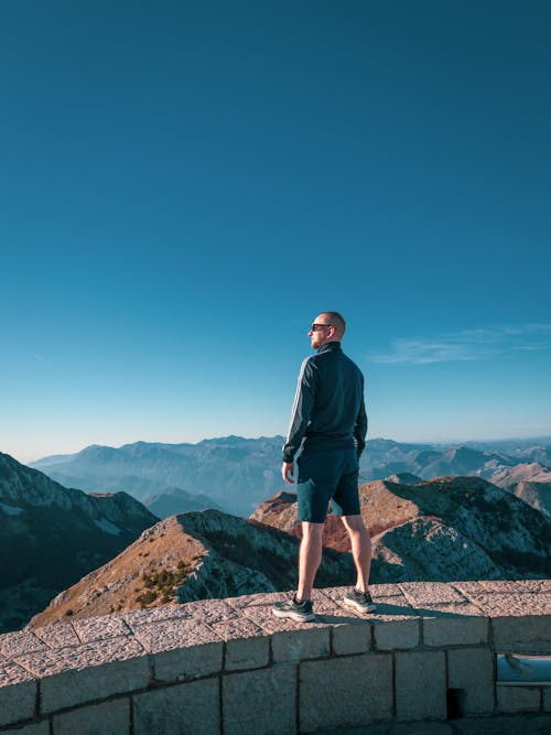 Man Standing on Top of a Mountain and Looking at the View 