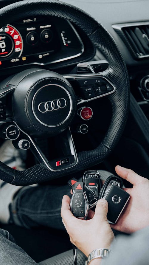 Free Person Holding Car Keys Sitting Behind a Black Leather Steering Wheel Stock Photo
