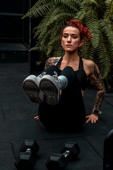 Tattooed woman with dyed hair performing workout indoors, emphasizing strength and fitness.