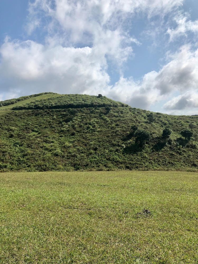 Green Grass Field And Mountain Under White Clouds