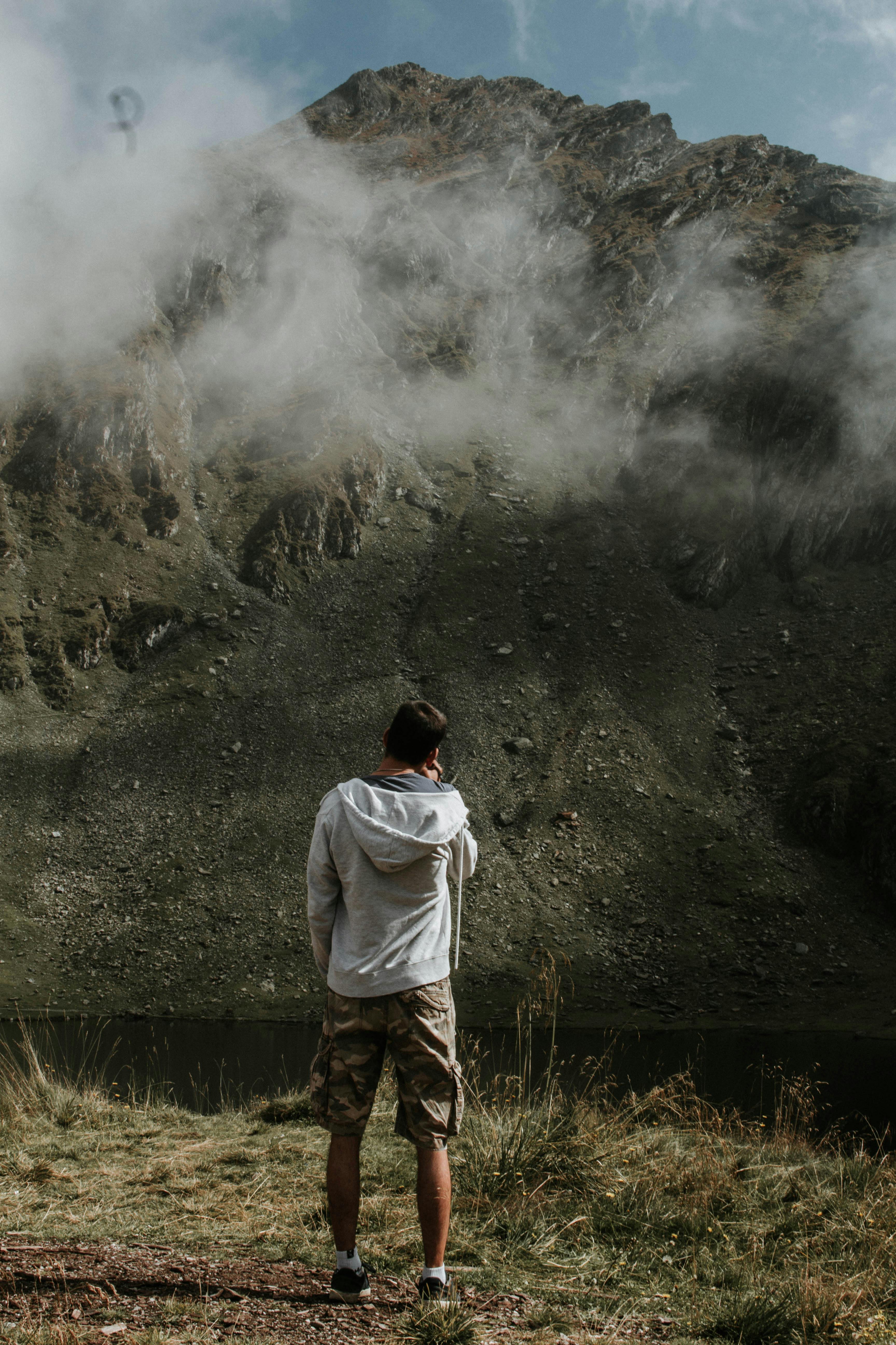 一名男子穿着休闲装，站在被雾笼罩的宁静山峰旁