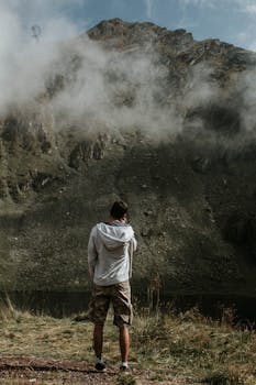 一名男子穿着休闲装，站在被雾笼罩的宁静山峰旁