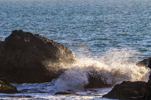 Free Dynamic waves crashing against dark rocks on a sunny coastal day, creating foamy splashes. Stock Photo