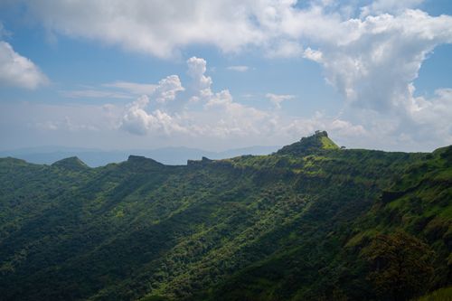 Free A scenic landscape view of lush green mountains and Rajgad Fort under a vibrant blue sky. Stock Photo