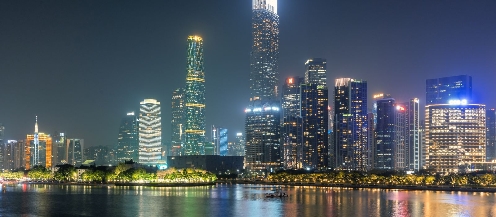 Illuminated skyscrapers of Guangzhou reflecting on the water under a night sky.