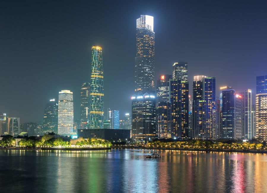 Illuminated skyscrapers of Guangzhou reflecting on the water under a night sky.