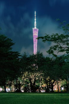 Stunning view of the illuminated Canton Tower rising above trees in Guangzhou, China at night.