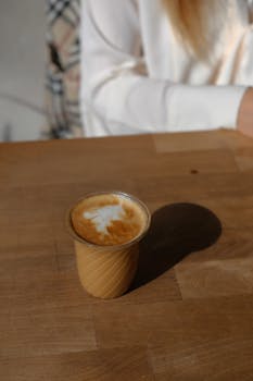 A freshly brewed cappuccino with latte art on a wooden table in sunlight, creating a cozy ambiance.