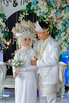 Beautiful Asian couple in traditional wedding attire with floral backdrop.