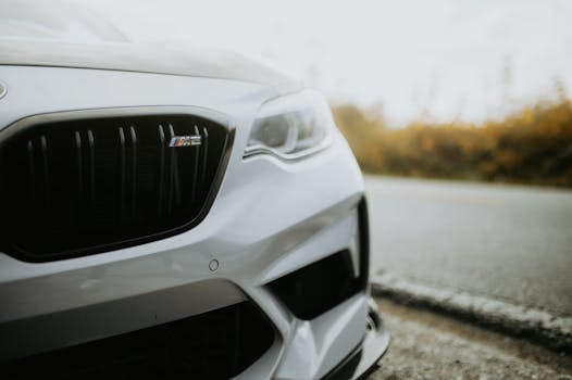 Detailed close-up of a shiny white sports car's front emblem and grill on the side of a road.