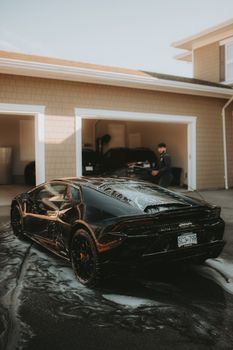 A sleek Lamborghini sports car getting washed in a driveway with a person nearby.