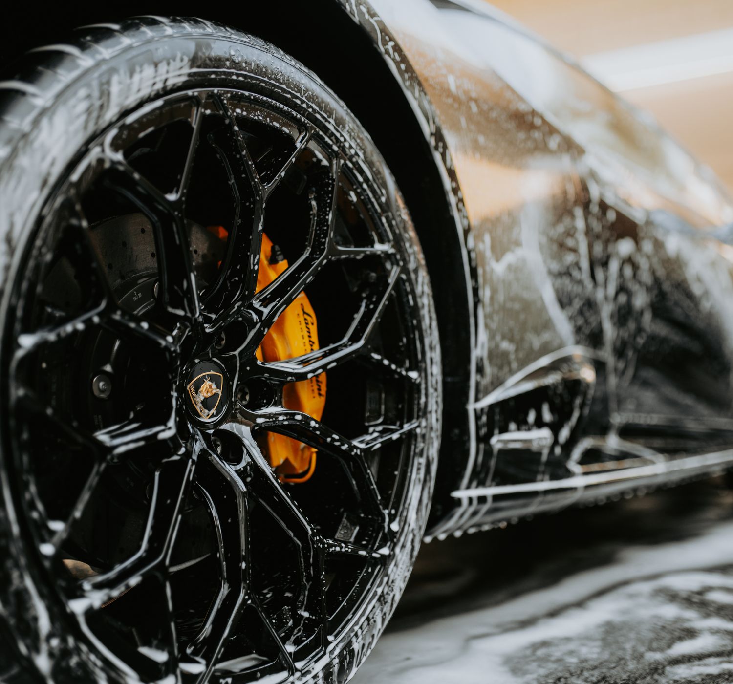 Detailed close-up of a luxury car wheel covered in soap suds during a professional car was