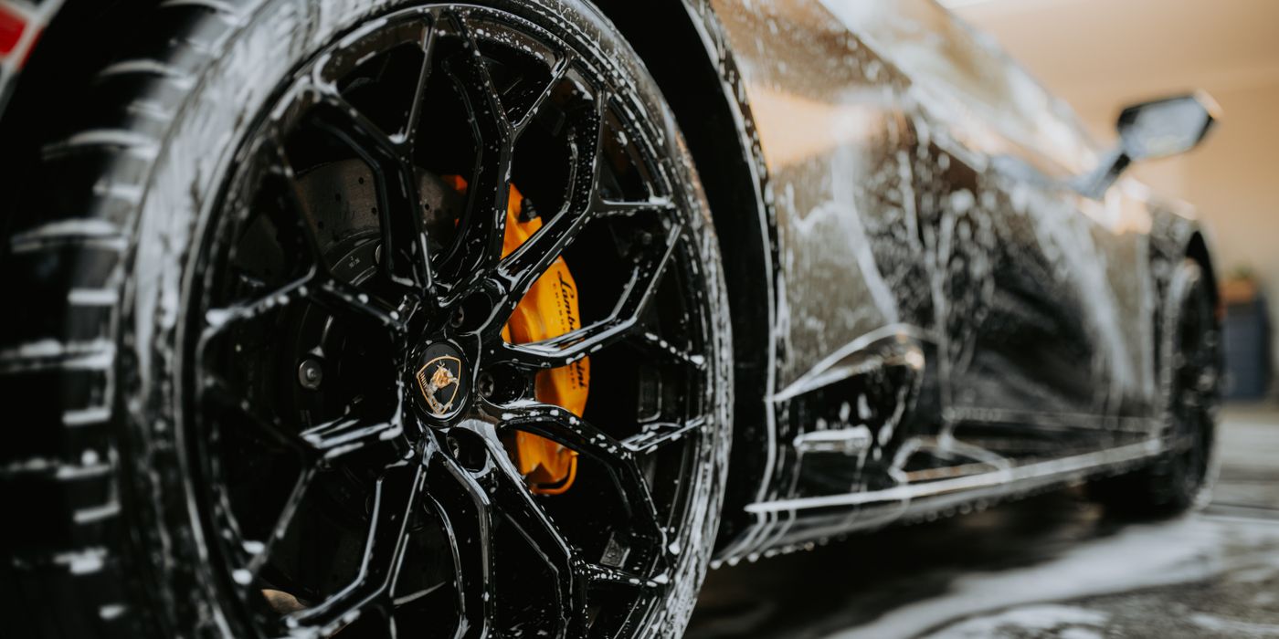A black sports car wheel covered in soap during a wash