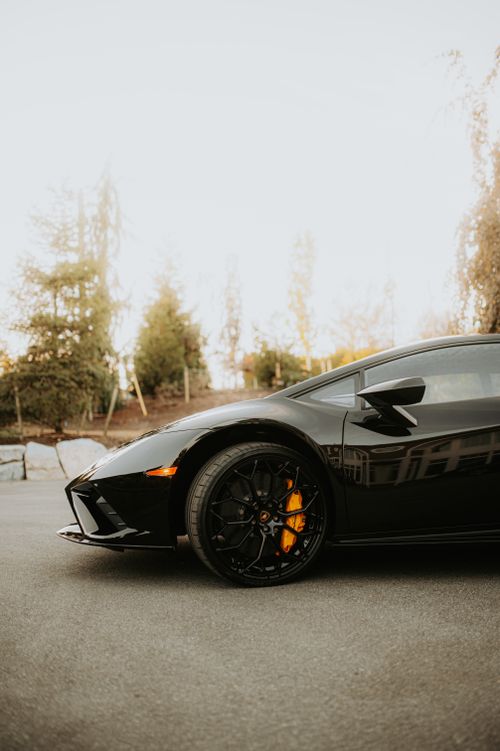 Free Sleek black sports car with unique rims and vibrant brake calipers in an outdoor setting. Stock Photo