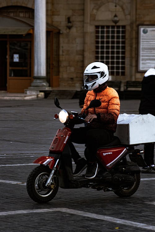 Person in Orange Jacket Riding Red Motor Scooter