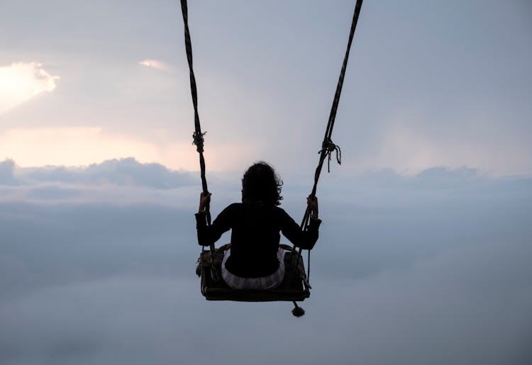 Woman Swinging On Swing Above Clouds