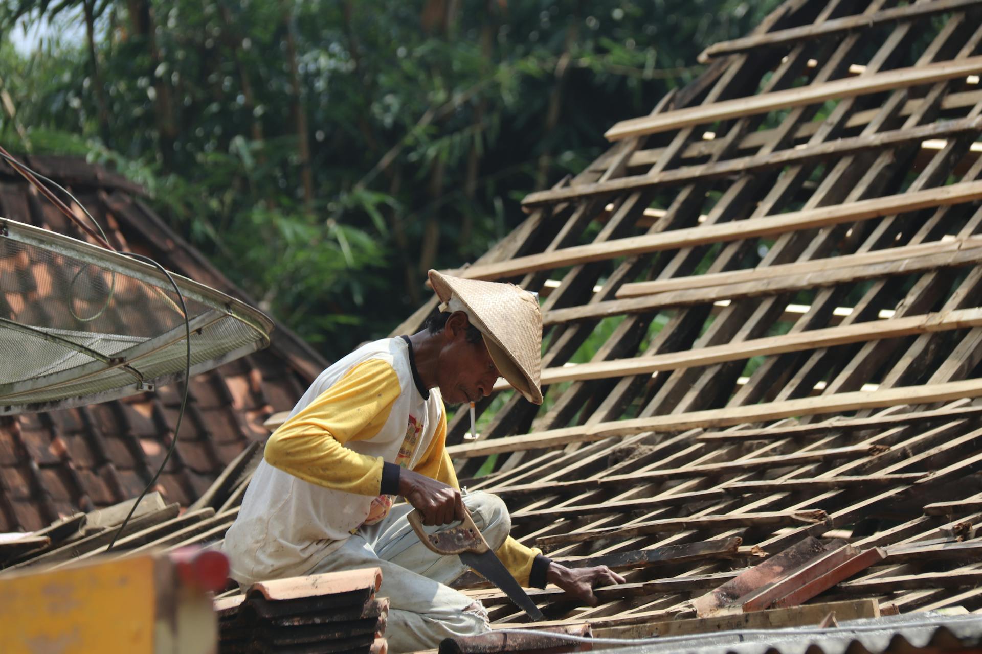 Carpenter working on a wooden roof structure outdoors in a rural setting with traditional tools.