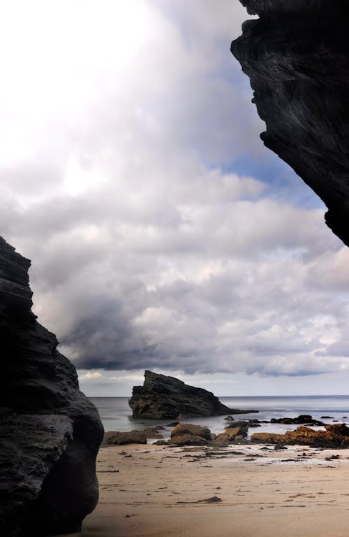бесплатная Скалы на берегу под белыми облаками и голубым небом Стоковое фото
