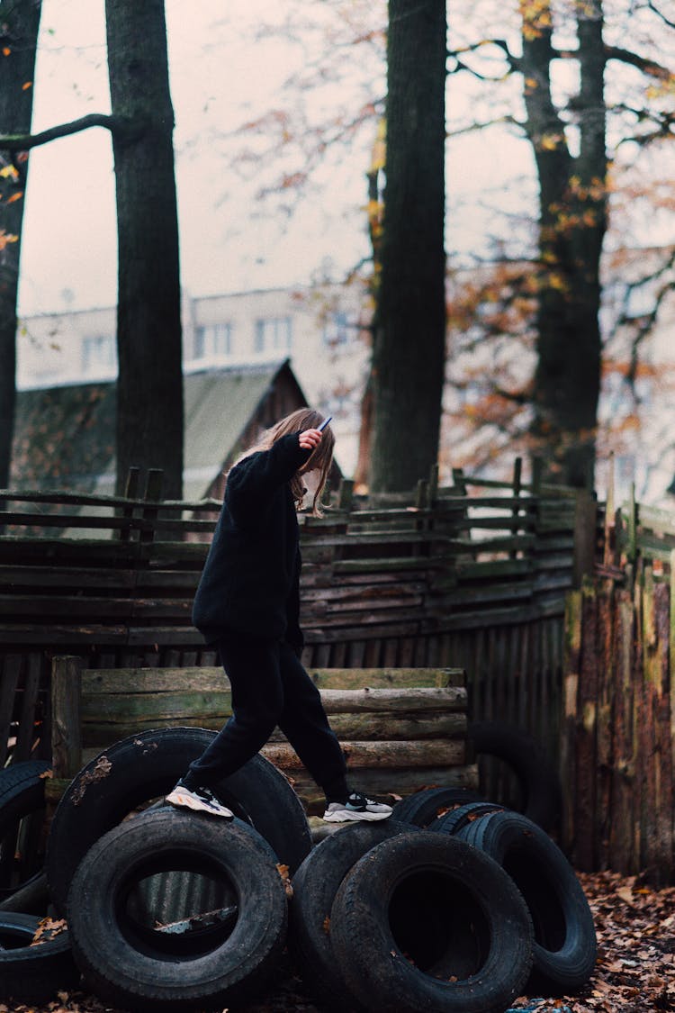 Young Girl Walking On Pile Of Tires In Yard