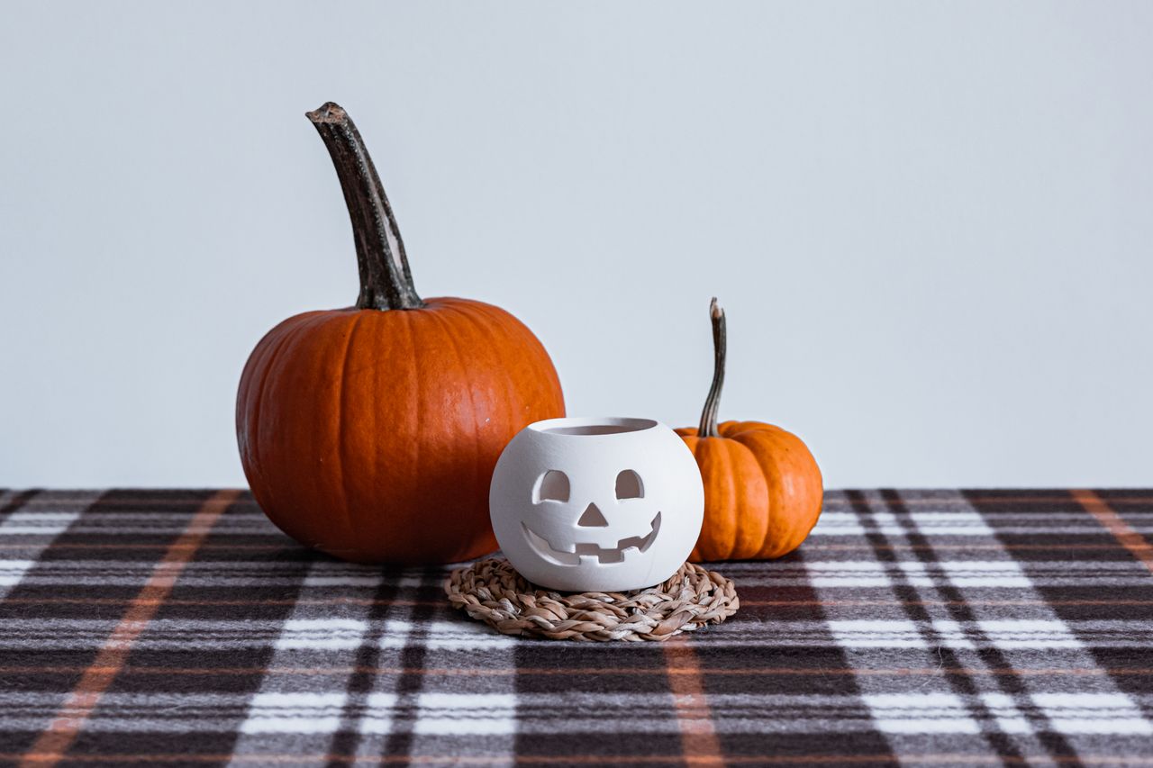 Orange pumpkins and a white ceramic jack-o-lantern on a black plaid table runner