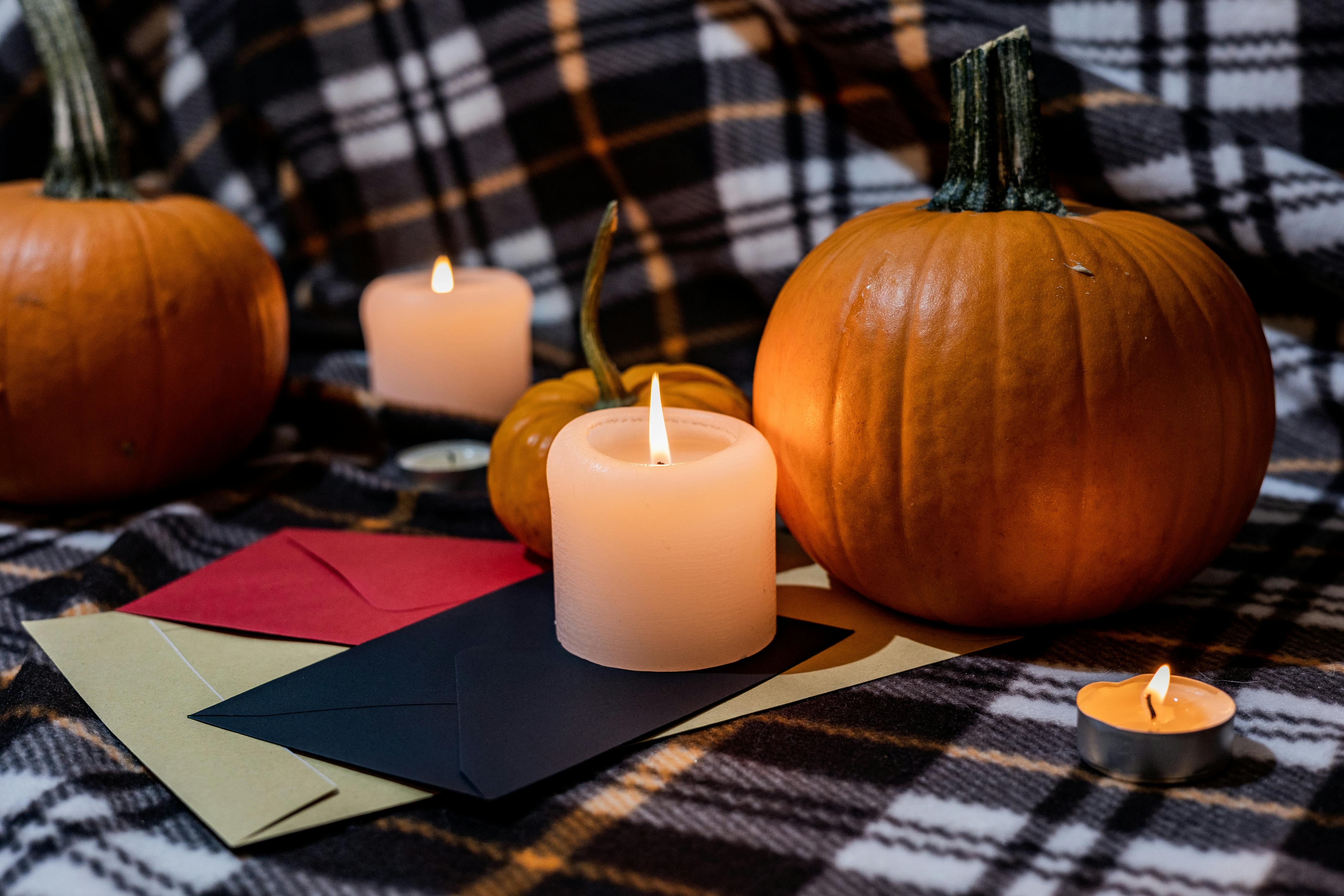 Warm Halloween scene with pumpkins, candles, and envelopes on plaid background.