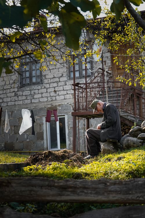 Free Elderly man sitting outside a rustic stone house in Tkibuli, Georgia, reflecting a serene lifestyle. Stock Photo