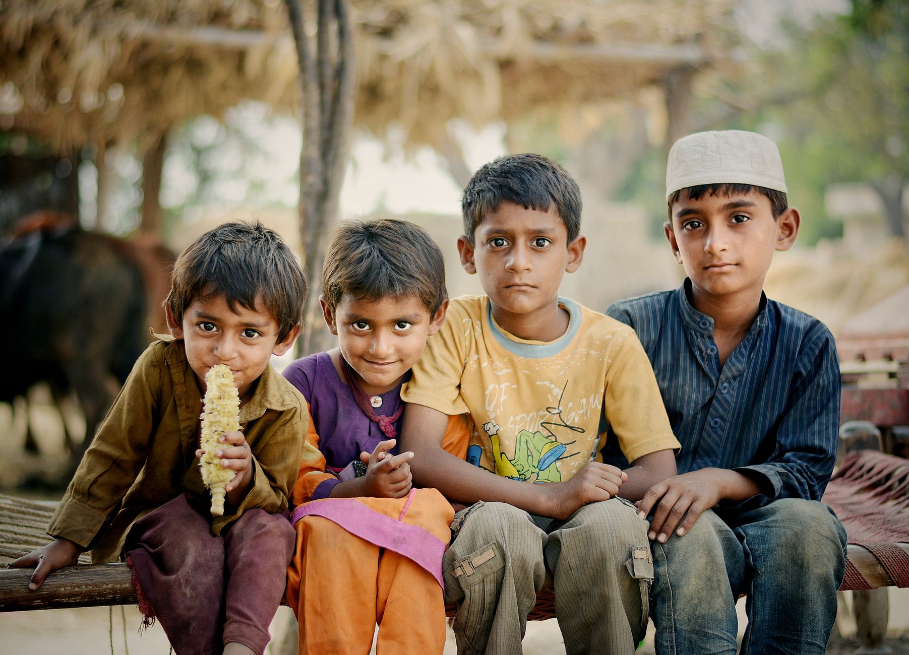 Four young children sitting together outdoors, enjoying each other's company.