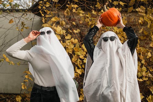 People Dressed as Ghosts Standing Outside and Holding a Pumpkin 