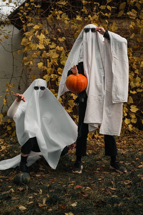 People Dressed as Ghosts Standing Outside and Holding a Pumpkin 