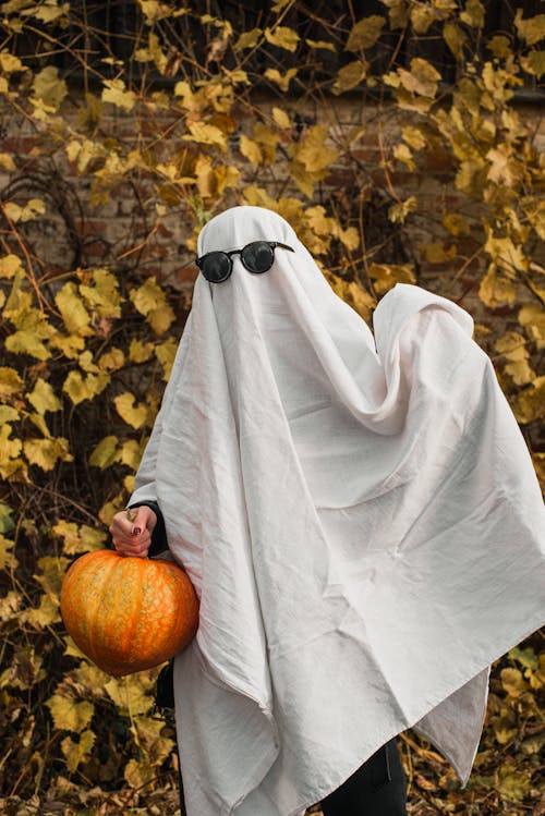 A Person in White Ghost Costume Holding an Orange Pumpkin