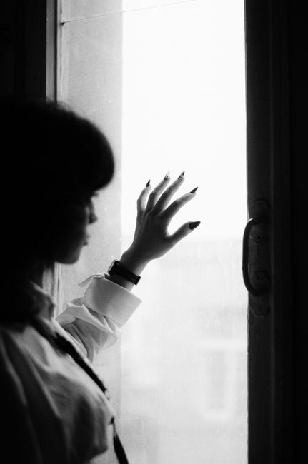 Black and white photo of a woman reaching towards a window, creating a silhouette effect.