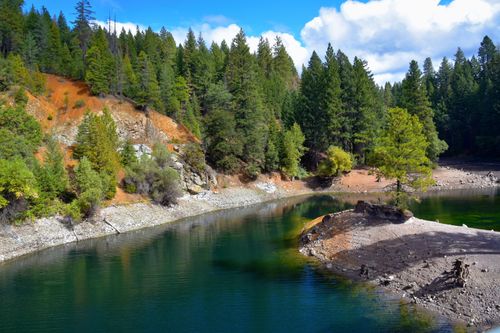 Free Discover serene beauty with this vibrant lake surrounded by lush evergreen forest and clear blue skies. Stock Photo