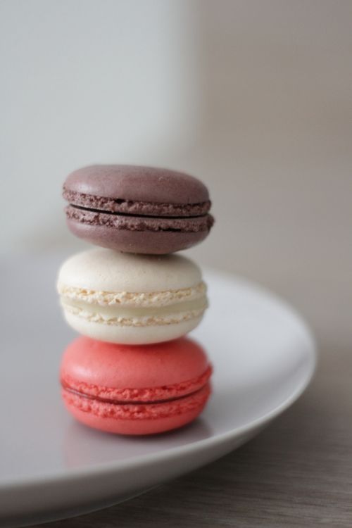 Free A close-up of three colorful French macarons stacked on a white plate. Stock Photo