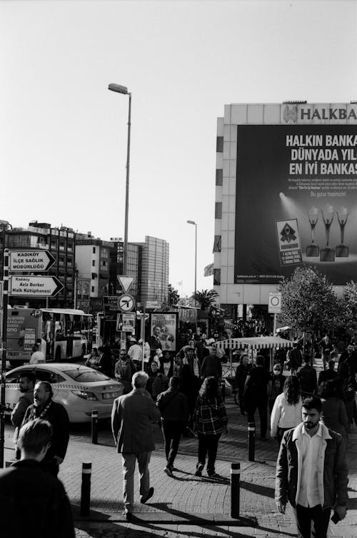 Grayscale Photo of People Walking on Street Near City Buildings