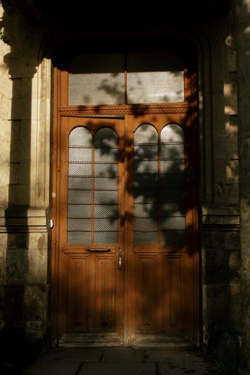 Free A classic wooden doorway with glass panels, framed by stone walls and textured shadows. Stock Photo
