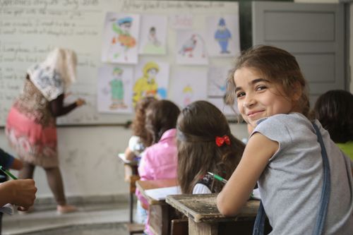 Free Smiling young girl in classroom, engaged in learning with colorful drawings on the board. Stock Photo