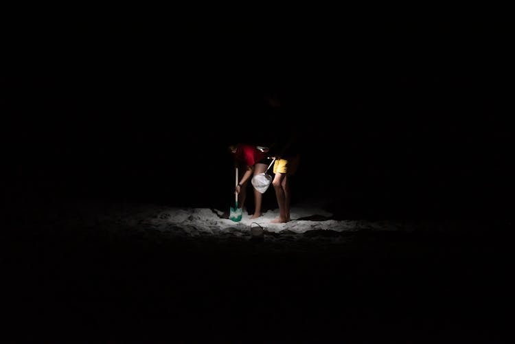 Two People Digging On A Beach At Night 