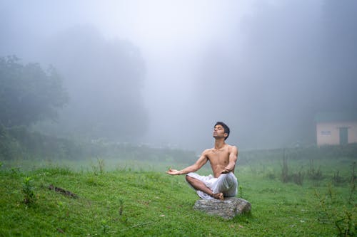A Man Sitting on the Stone in the Grassland in Lotus Position