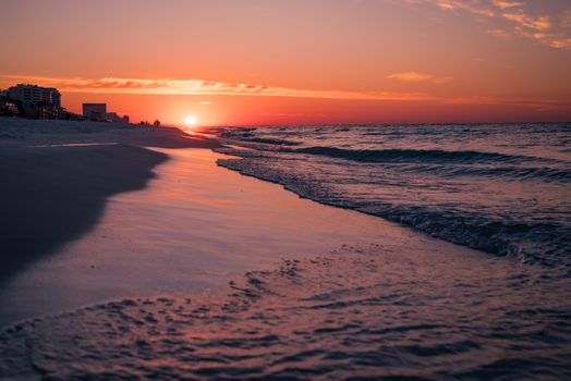 A breathtaking view of a beach at sunset with reflective waves and a vibrant sky.