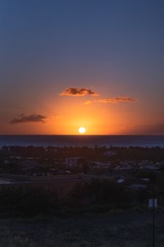 Stunning sunset view over an ocean horizon with vibrant colors and silhouetted townscape.