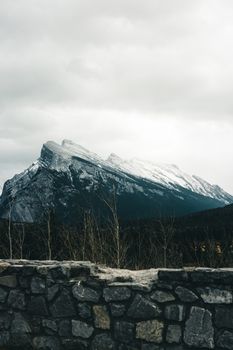 Serene winter landscape of snow-capped mountains in Banff National Park with a stone wall in the foreground.