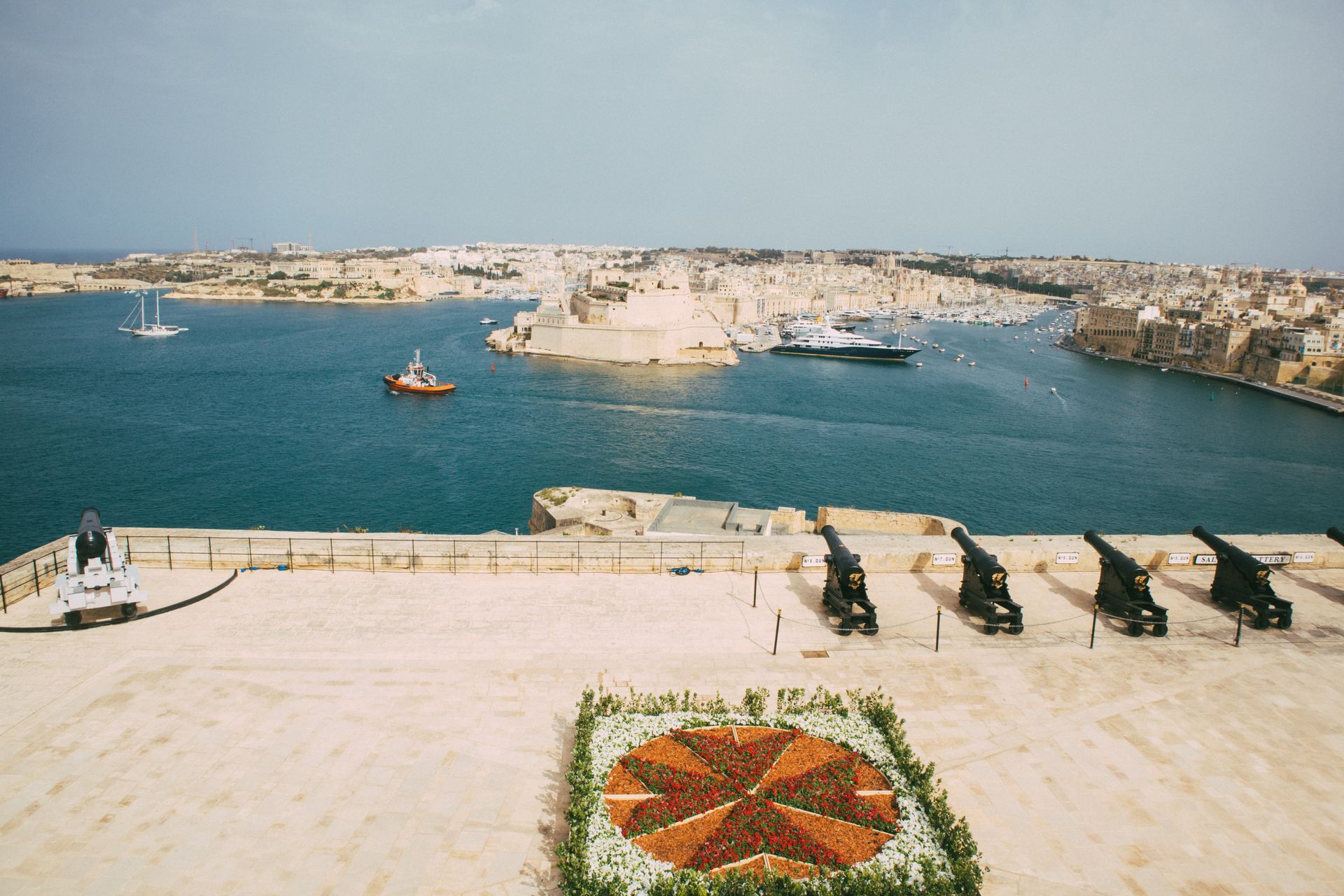 Aerial view of the Saluting Battery and Grand Harbour in Valletta, Malta, showcasing cannons and waterfront.